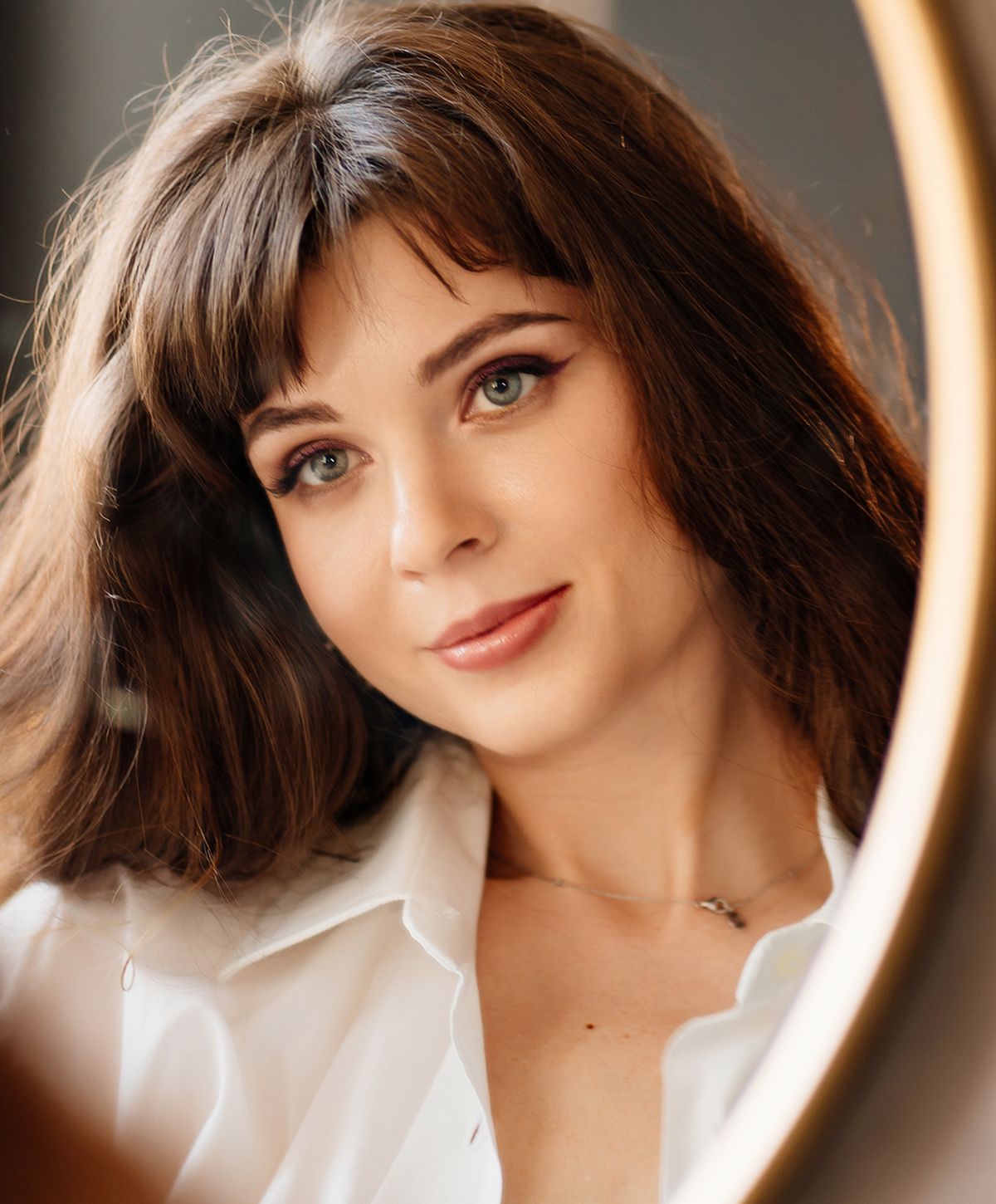 Woman with brown hair posing by mirror.