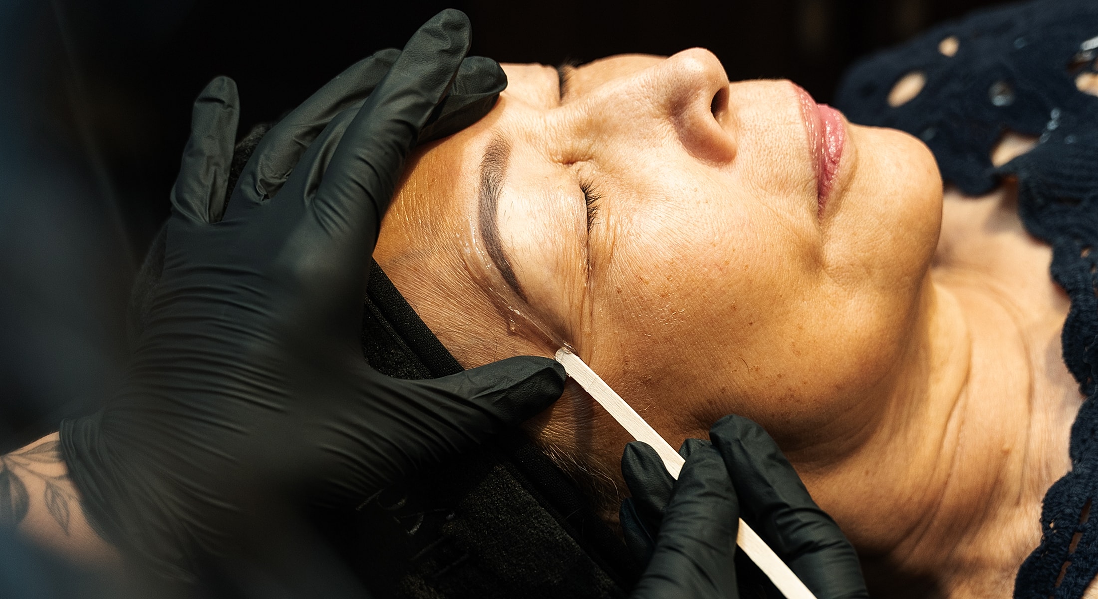 Woman receiving skincare treatment with gloved hands.
